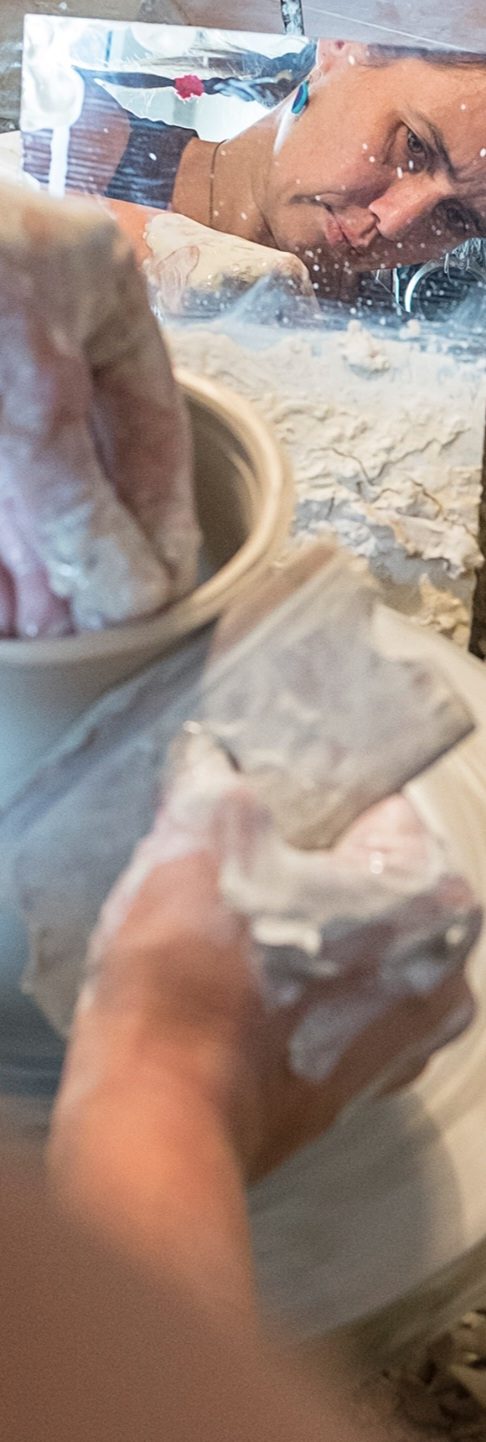 töpfern an der Scheibe Hände mit Keramikmasse und einem Tontopf auf einem Tisch beim Arbeiten.