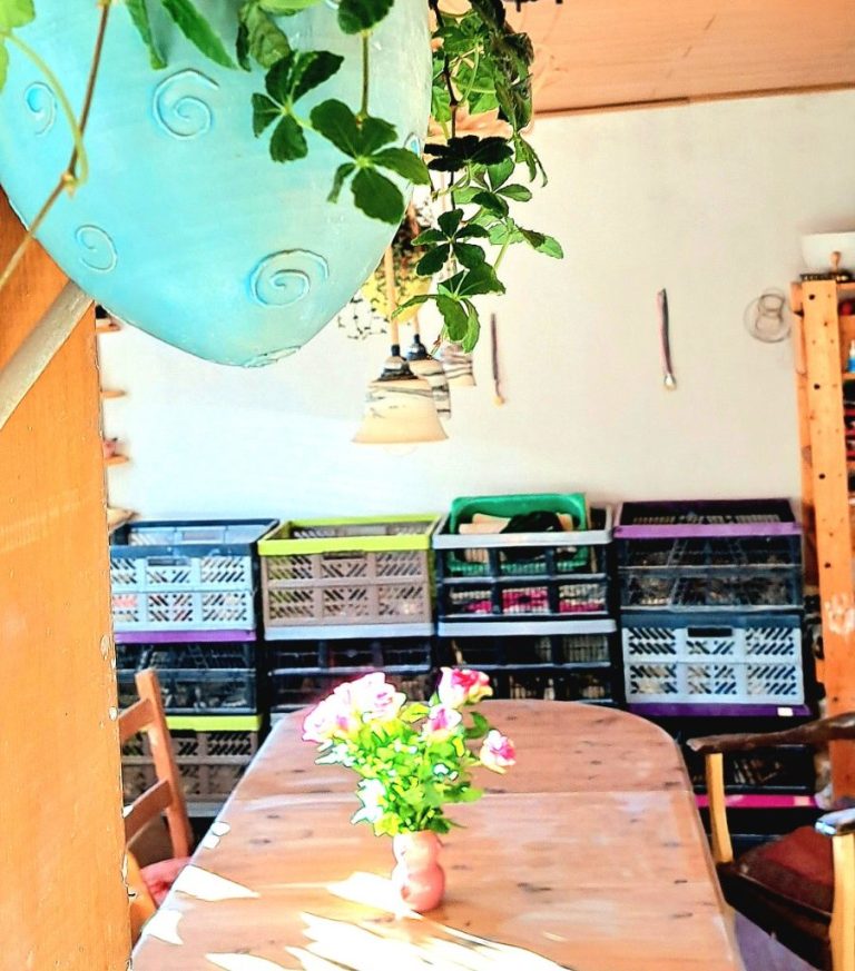 Töpferei mieten Ein helles Zimmer mit einem Holztisch, Vasen mit Blumen und Regalen im Hintergrund.